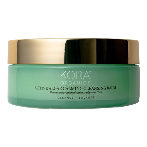 100g glass jar of KORA Organics Active Algae Calming Cleansing Balm, a cleanser with microalgae, pineapple enzymes, jojoba and squalane that cleanses away makeup, dirt and oil for a clearer, more balanced complexion. Packaged in a green glass jar with a gold lid.