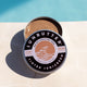 Open tin of tinted mineral (non-nano zinc oxide) SPF50 sunscreen perfect for the face placed by a swimming pool.