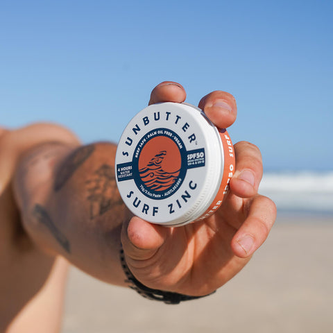 Person holding tin of tinted vegan surf zinc with SPF50.