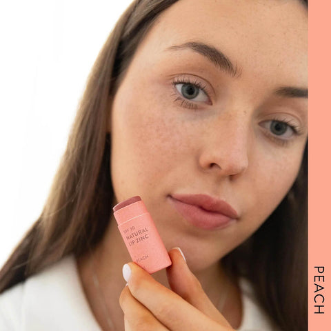 Model wearing Winki Zinc's Tinted Lip Zinc in the shade, Peach, a classic, summery pink. Perfect for a pop of colour on the lips and cheeks (medium pigment). Tinted Lip Zinc is a mineral-based lip balm designed to heal and protect your lips from the sun while adding a hint of natural colour.